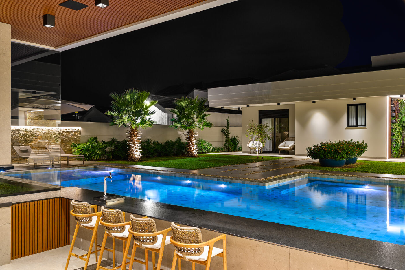Piscina iluminada com cadeiras na borda à noite – projeto i9 Arquitetura